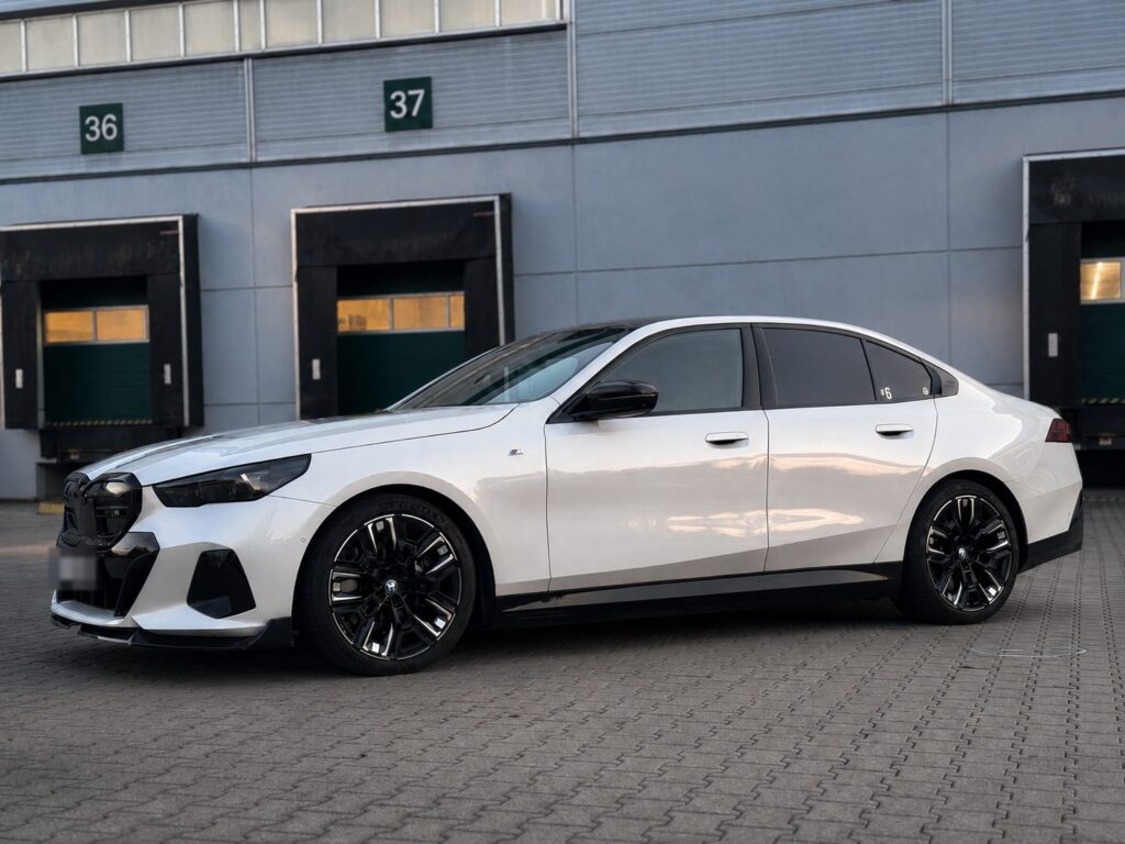 Bílé BMW i5 M60 xDrive z boku před halou s nakládacími rampami