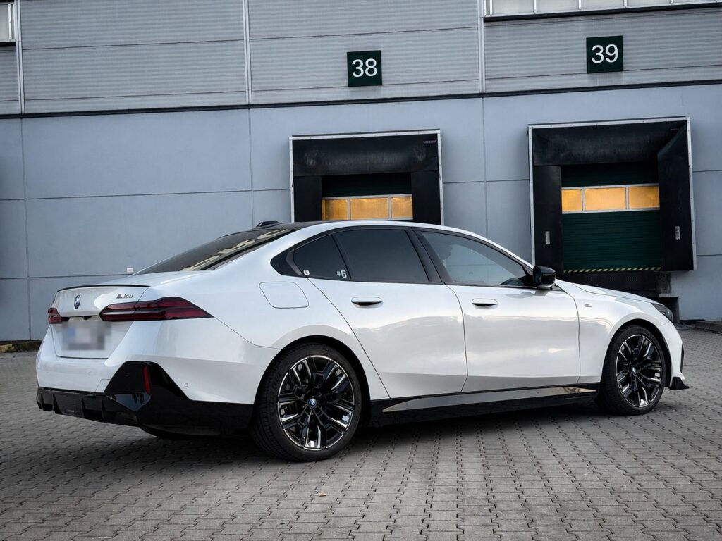 Bílé BMW i5 M60 xDrive zezadu z boku před halou
