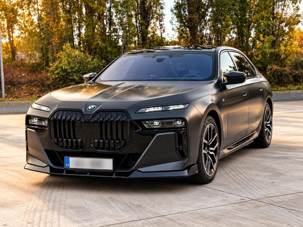 Přední část matně šedého BMW i7 xDrive60 G70 na parkovišti s podzimními stromy
