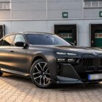 Matně šedé BMW i7 xDrive60 G70 zepředu z boku před logistickou halou