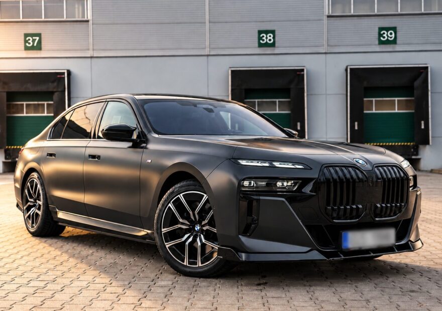 Matně šedé BMW i7 xDrive60 G70 zepředu z boku před logistickou halou